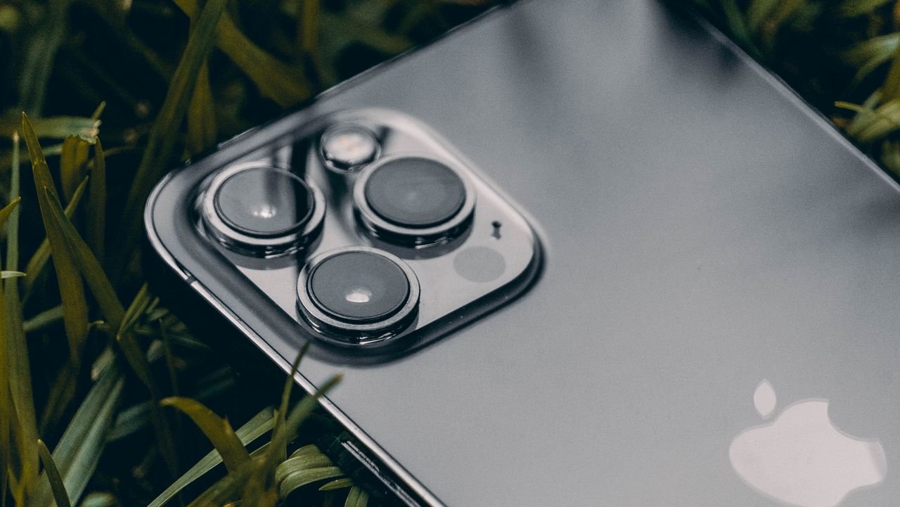 Macro shot of a smartphone with a triple camera system on leafy grass, showcasing modern technology.
